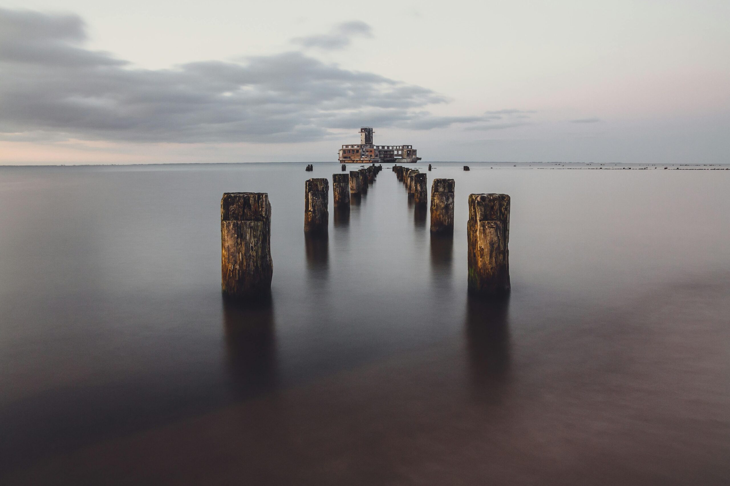 Tranquil sunset view of sea fort ruins near Gdańsk, Poland with weathered wooden pilings in the foreground.